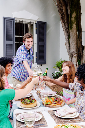 Group of multi ethnic friends having fun celebrating toasting with champagne at an outdoor garden partyの写真素材