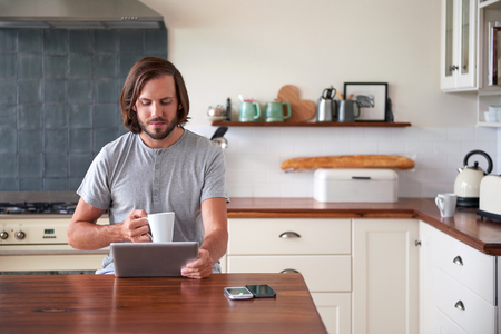 young man enjoying morning coffee with tablet computer in home kitchenの写真素材
