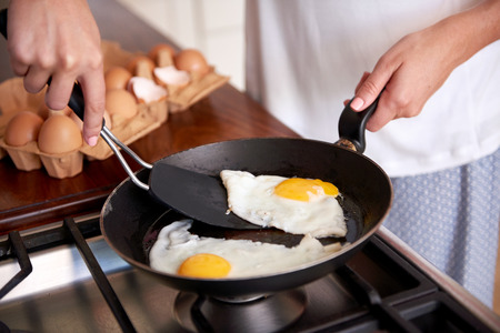 woman preparing early morning eggs breakfast on stove in home kitchenの写真素材