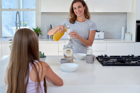 Beautiful Caucasian mother with her daughter girl child in the kitchen for breakfast orange juice candid momentの写真素材