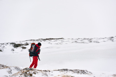 Man in full winter gear and backpack hiking in the snow exploring the all white natural landscape