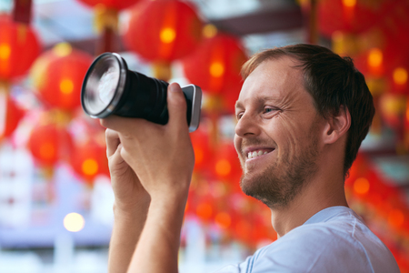Candid portrait of a caucasian tourist taking a photo picture in china town with red traditional oriental lanterns in modern asian cityの写真素材