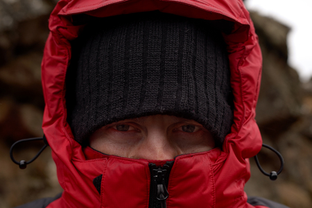 Close up portrait of an active outdoors man protected covered by beanie and hood to fight the cold extreme harsh conditionsの写真素材