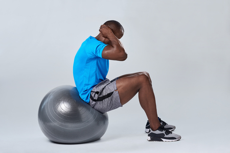 Fit healthy man uses pilates gym fitness ball as part of toning and core muscle building training exercisesの写真素材