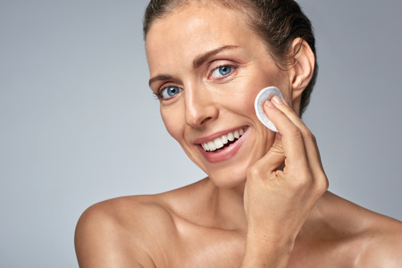 Smiling middle age woman wiping cleaning her face with cotton wool, wellness beauty skin care conceptの写真素材