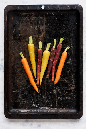 Bunch of baby heirloom carrots on dark vintage distressed baking tray, food backgroundの写真素材