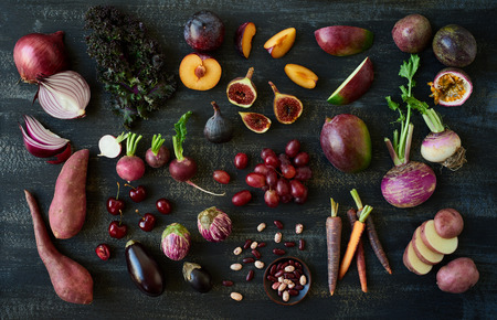 Collection of fresh purple toned vegetables and fruits on dark rustic distressed background, eggplant, turnip, mango, carrot, fig, aubergine, grapes, radishes, kale, kidney beans, plum, passionfruit, cherriesの写真素材