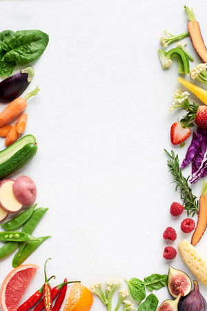 Food background border flatlay of rainbow coloured fresh fruits and vegetables, carrot chilli cucumber purple cabbage spinach rosemary herb, plenty of copy-space