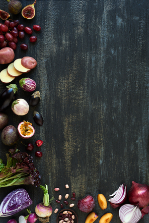 Collection of fresh purple toned vegetables and fruits on dark rustic distressed background, eggplant, onion, plum, carrot, fig, aubergine, grapes, radishes, loose leaf lettuce, beans passionfruit, cherriesの写真素材