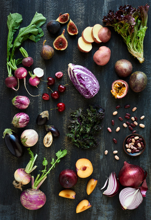 Collection of fresh purple toned vegetables and fruits on dark rustic distressed background, heirloom eggplant, fig, aubergine, cherries, radishes, lettuce, beans passionfruit, cabbage, plum, onionの写真素材