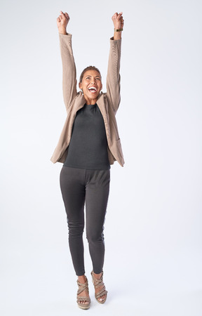 Full length portrait of mixed race woman celebrating with arms up isolated on greyの写真素材