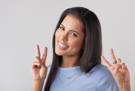 Headshot of pretty woman making hand gesture peace sign, like a tourist posingの写真素材