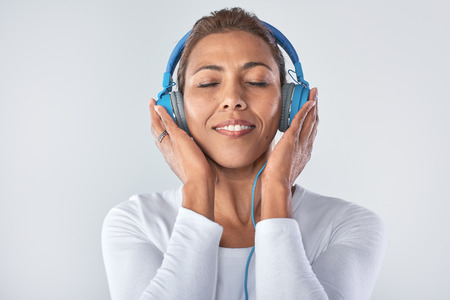 Headshot of mature woman enjoying listening to music with large headphones in studioの写真素材