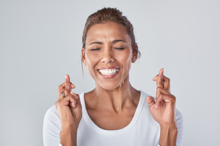 Headshot of mixed race woman wishing hoping with fingers crossed, expressionsの写真素材