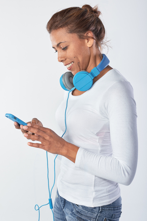 Mixed race woman with large headphones choosing music on her phoneの写真素材