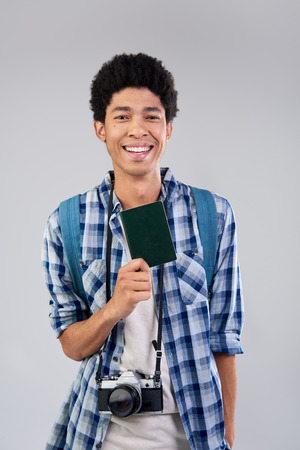 Young mixed race tourist man with afro holding passport visa and camera on his way to travel adventureの写真素材