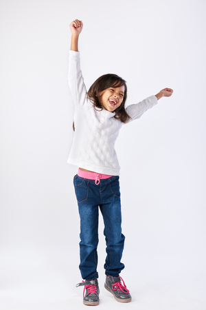 young girl celebrating with arms up and jumping isolated on white backgroundの写真素材