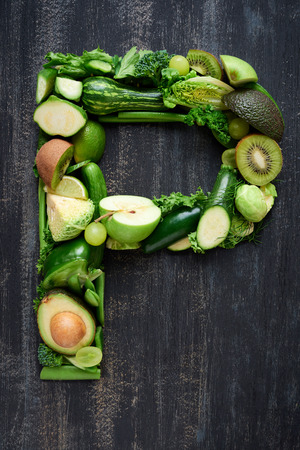 overhead flat lay display of green fruit and vegetables arranged in alphabet letter shapes, for design websites postersの写真素材