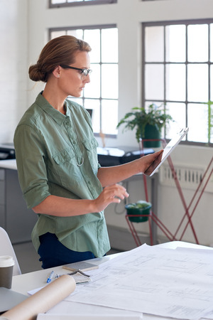 Professional architect interior designer making material choices on her tablet device, blueprints and drawings on the tableの写真素材