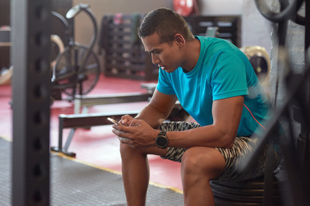 Healthy man using fitness exercise tracking app on smart phone in indoor gymの写真素材
