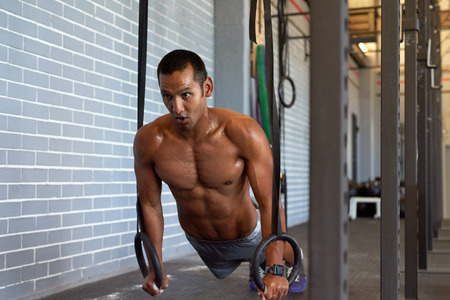Determined man working out in gym with gymnastic rings for strength and crossfit core exercise