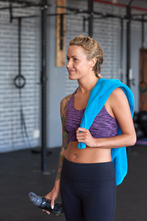 Smiling portrait of a fit healthy woman in sportswear holding exercise towel and bottle in gymの写真素材
