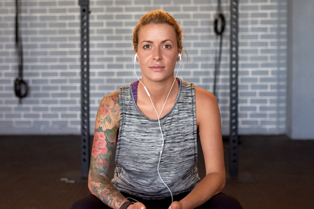 Portrait of woman with tattoos in gym wearing sportswear and earphones, confident and determinationの写真素材