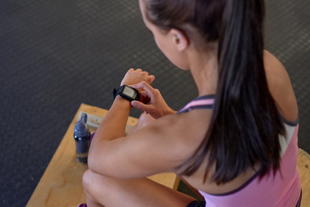 Sporty woman sitting and checking smart watch fitness activity tracker monitor isolated in gym before exerciseの写真素材