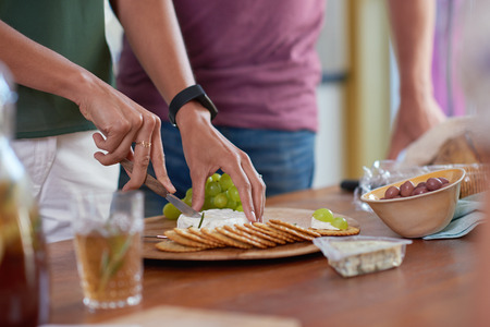 Woman hands cutting slicing cheese for appetisers platter starters in party with biscuits grapes and olivesの写真素材