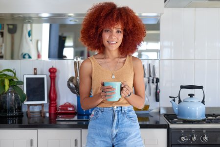 Happy smiling woman homeowner in cosy home kitchen holding coffee teaの写真素材