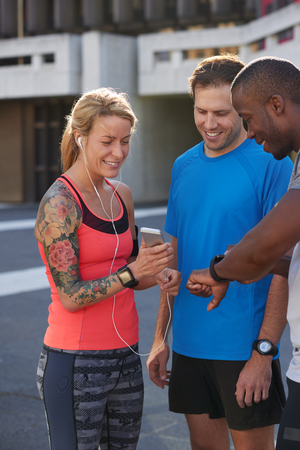 Sporty woman with tattoos shows her friends the new fitness app music playlist on her mobile phone wearable device technologyの写真素材