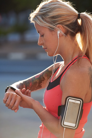 Fit athletic woman with tattoos tracking her run exercise progress with wearable technology watch mobile smartphone in urban cityの写真素材