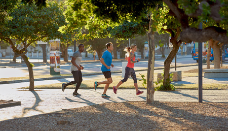 Urban running in the city, friends jogging exercising together between modern buildings and roads with sun flareの写真素材