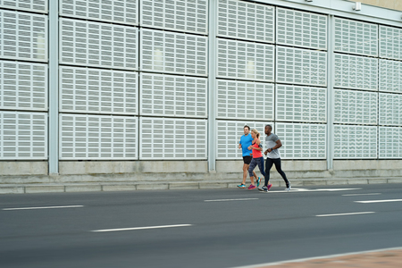 Fit athletic group of people running exercising together through urban landscape cityscapesの写真素材
