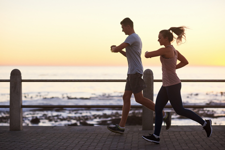 Couple looking at their fitness tracking app while running along the ocean at sunset, fit active lifestyleの写真素材