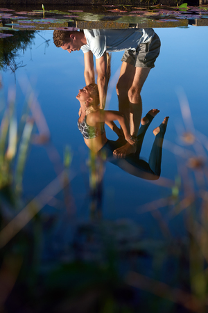 Artistic reflection on water of couple doing yoga together, strength trust exercise healthy lifestyleの写真素材