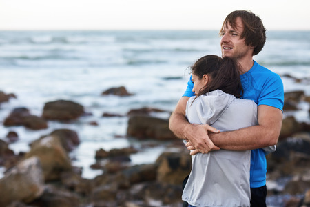 Couple in sportswear hugs affectionately on coast, enjoying the scenic view after their exerciseの写真素材