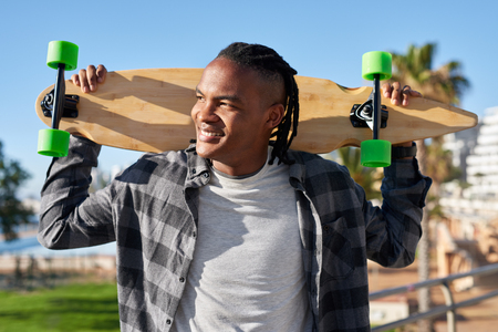Portrait of smiling mixed race man holding skateboard, carefree fun summer lifestyleの写真素材