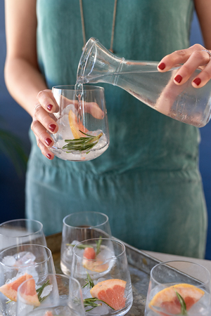 Festive celebration drinks woman at party making a tray of gin and tonics with rosemary and grapefruitの写真素材