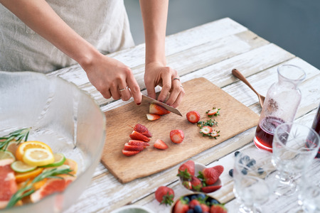Woman slicing fresh strawberries to add to the fruit punch cocktail mocktail for fourth of july partyの写真素材