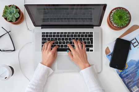 Overhead of work desk with woman typing replying to emails on laptop computer, freelance entrepreneur creativeの写真素材
