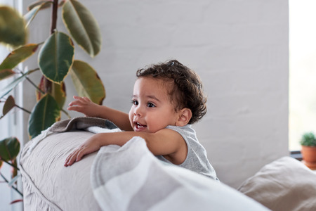 Candid portrait of a cute baby cruising, holding on to back of  couch sofaの写真素材