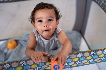 Portrait of cute baby boy in cot holding a toy block, childhood development educationalの写真素材