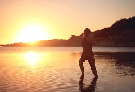 Woman doing yoga in shallow water at the bach during sunsetの写真素材