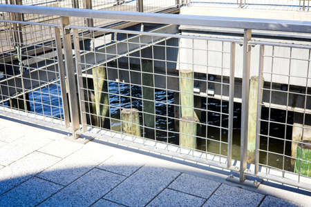 Pier with concrete walk and metallic fence over water and old abandoned wooden support logsの写真素材
