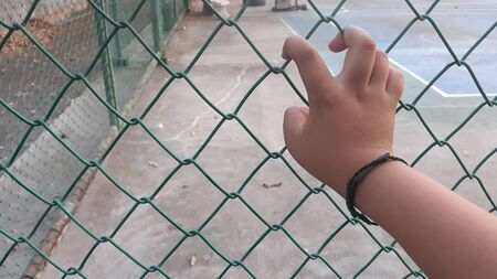Hand of fat boy push the net in the park. His fingers touch the net