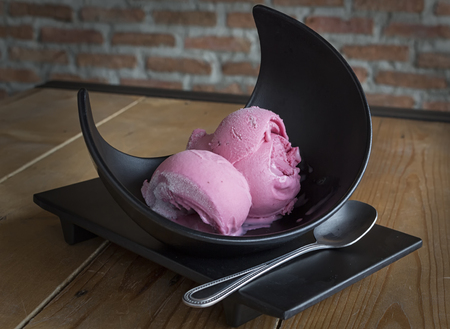 Rasberry ice-cream in black bowl on the wooden tableの写真素材