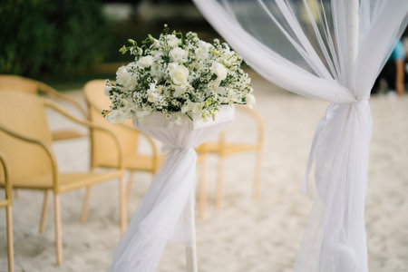 Bouquet of white roses and green leaves on the beach wedding arch.Wedding arch decorated with white flowers on a sandy beach.の写真素材