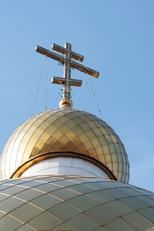 Cross on a gold dome of a temple on a background of the blue sky