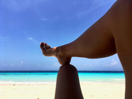 Close-up of a foot resting on a knee facing the sea on a beach in Zanzibarの写真素材